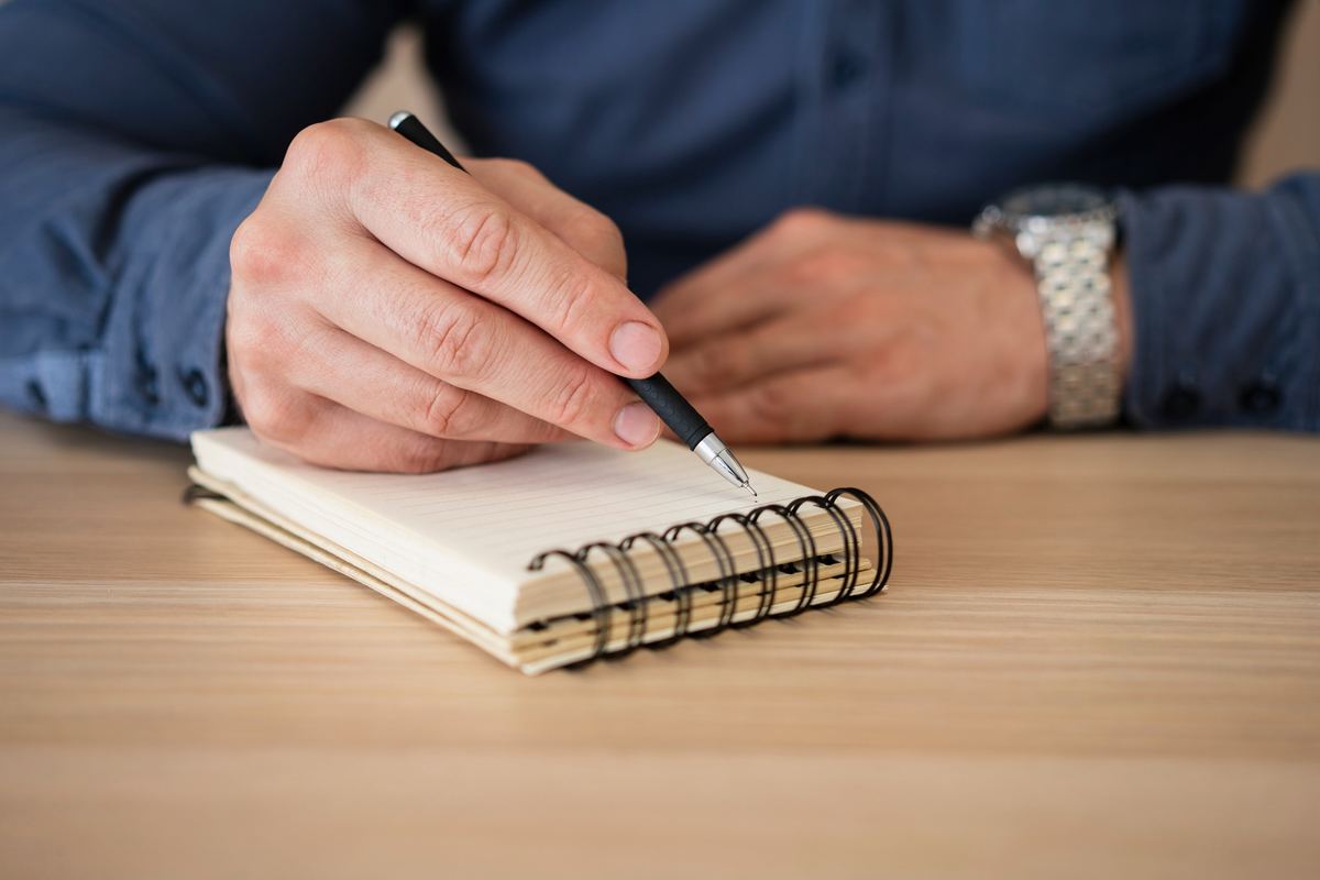 A hand writing notes in a spiral notebook